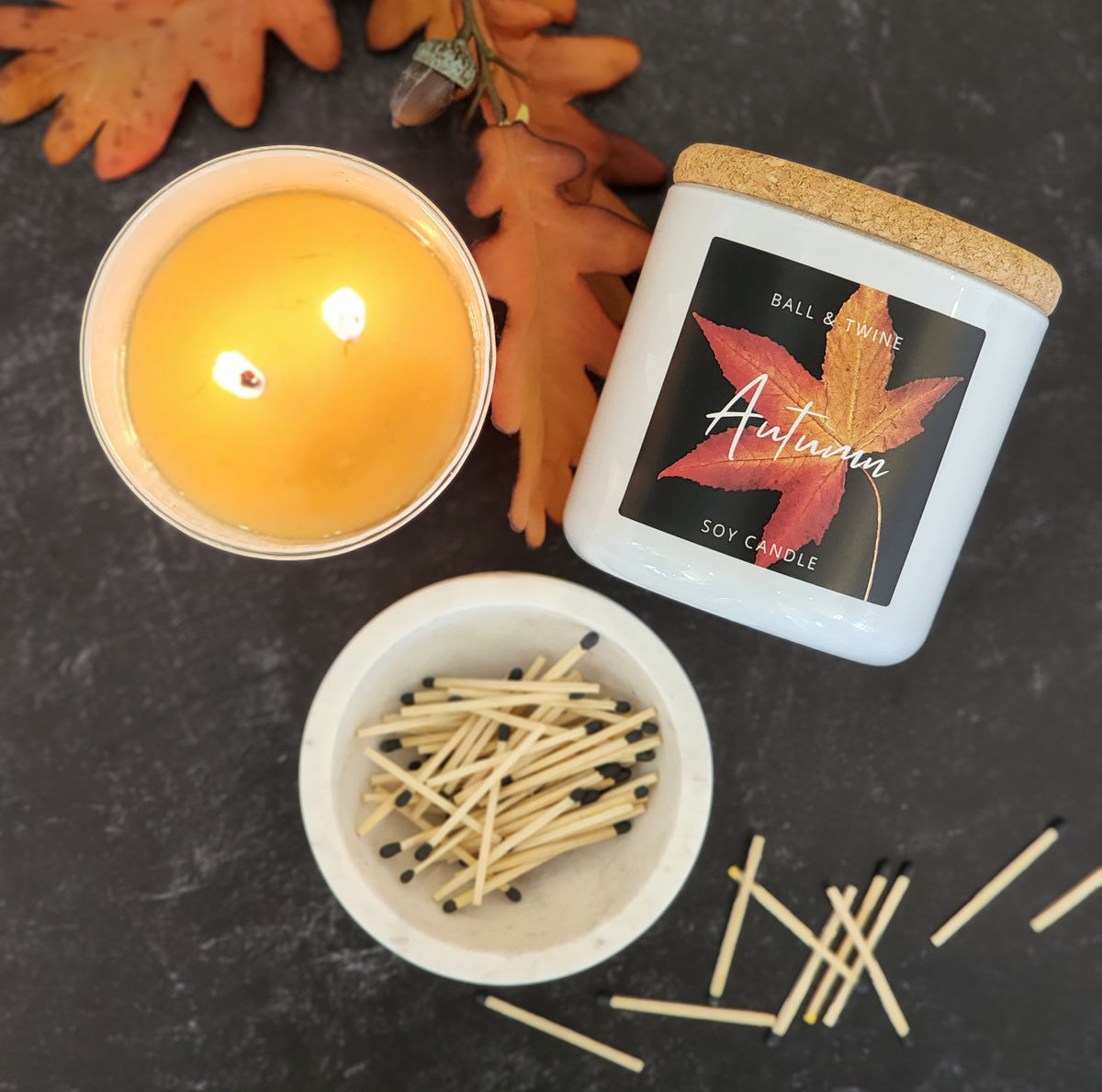 Autumn candle lit beside matches and oak leaves
